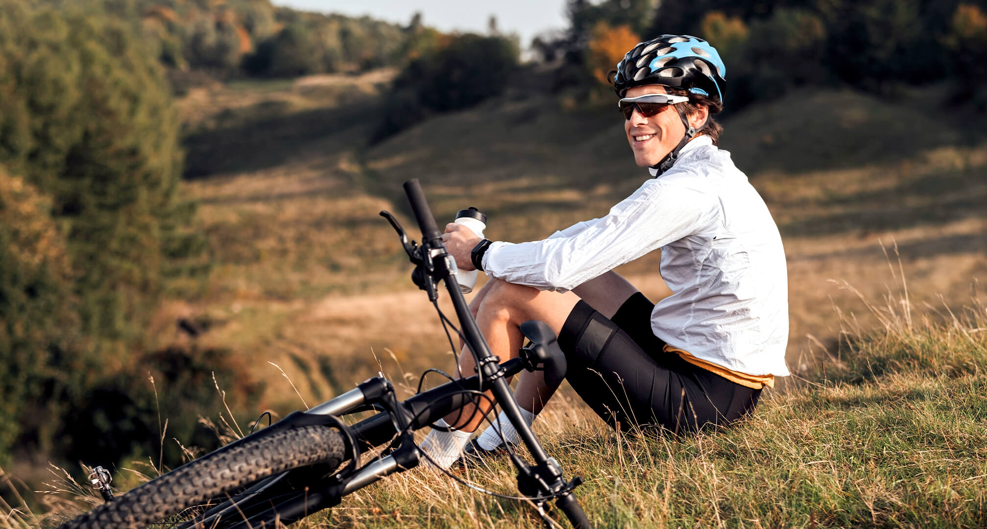 personne assise sur une colline avec un vélo de montagne et portant des lunettes de soleil